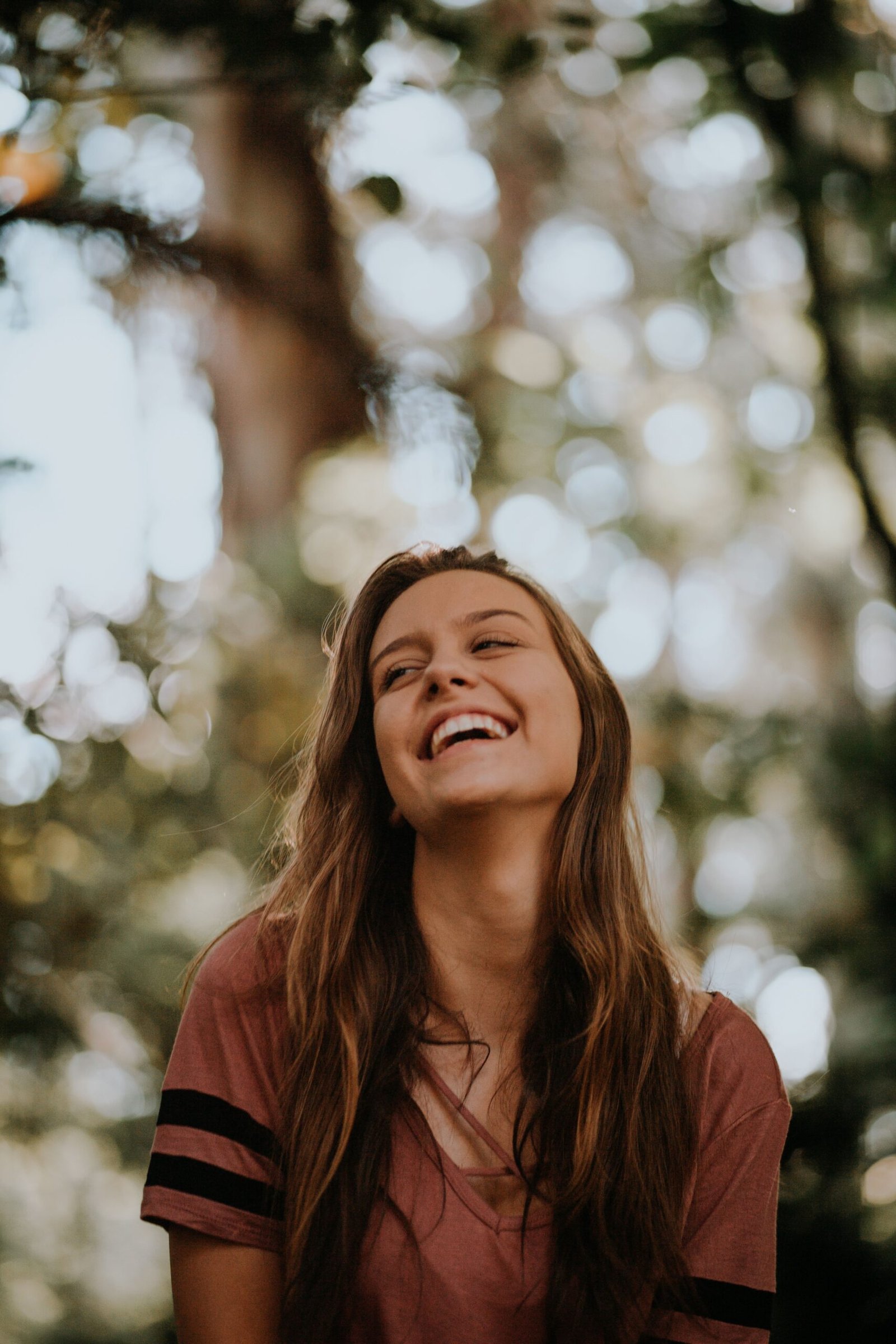 Woman laughing joyfully outdoors in dappled sunlight beneath trees
