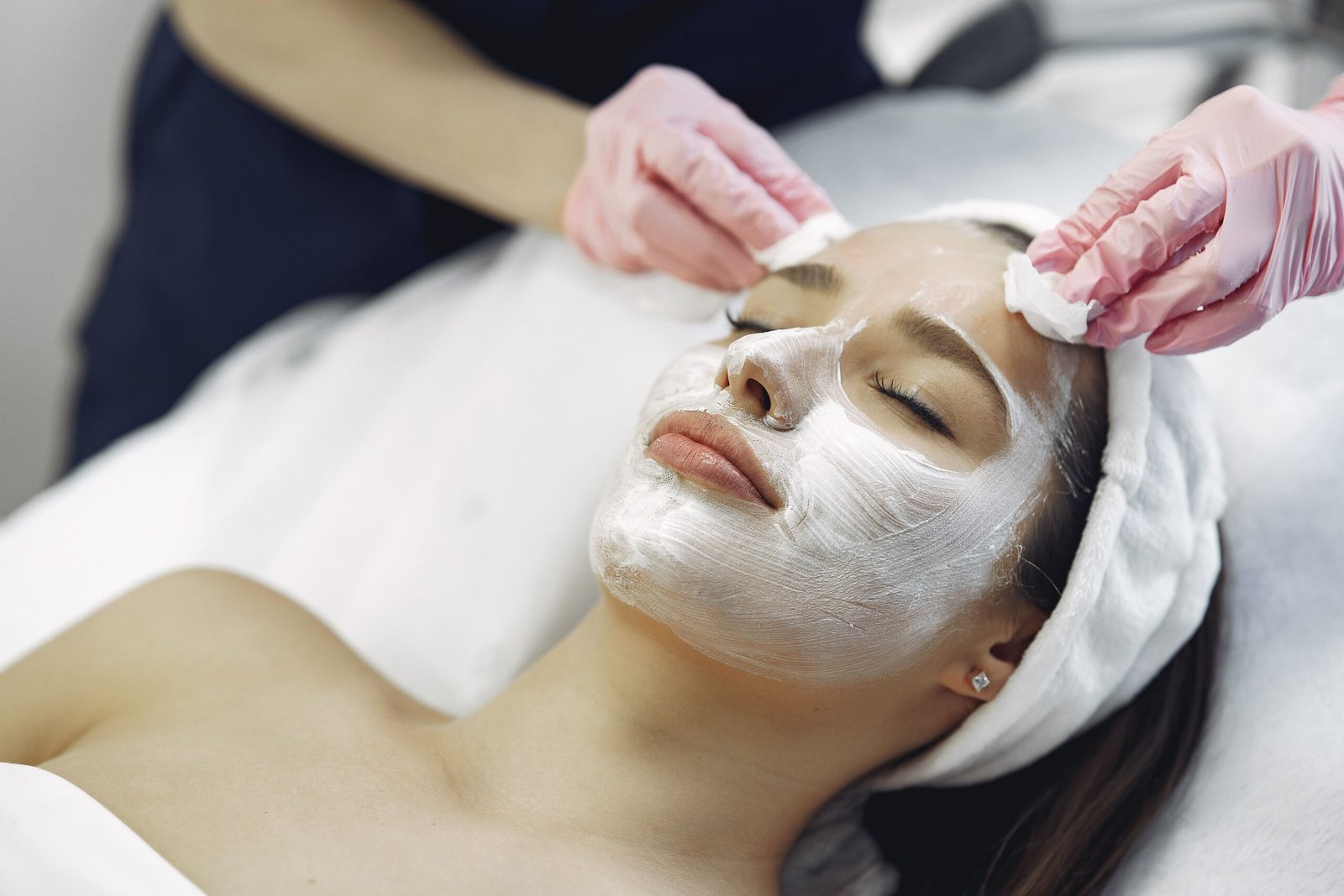 Esthetician removing a facial mask from a client's skin with cotton pads