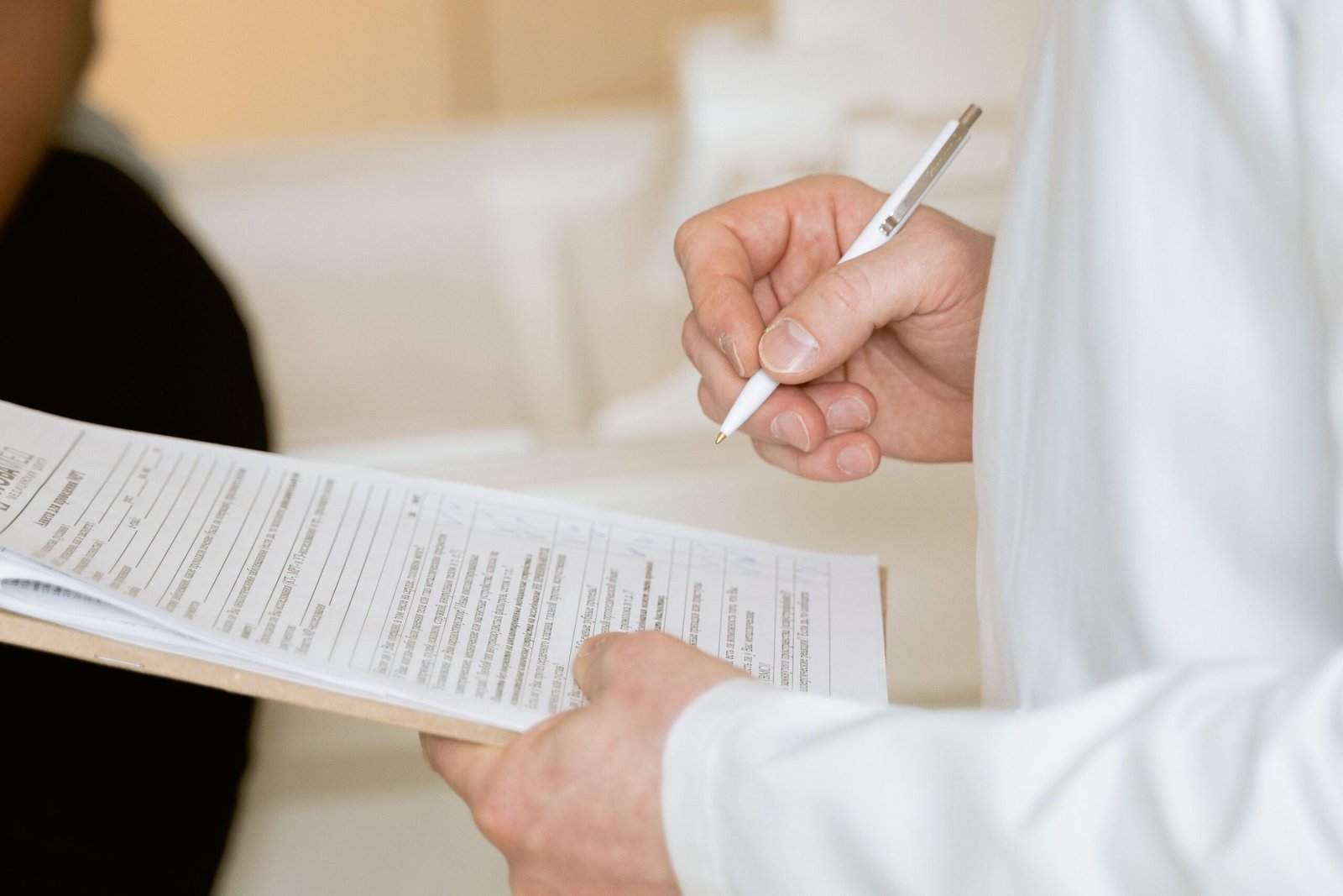 Provider in a white coat writing on a clinical intake form attached to a clipboard
