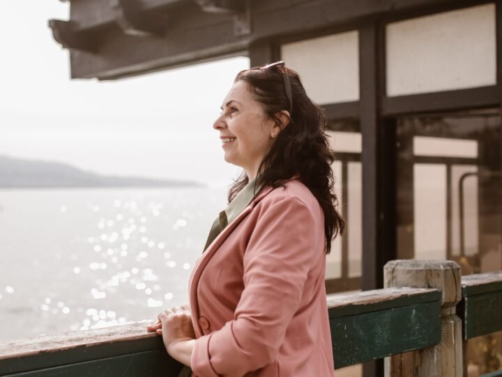 Smiling middle-aged woman in a pink coat looking out over the water