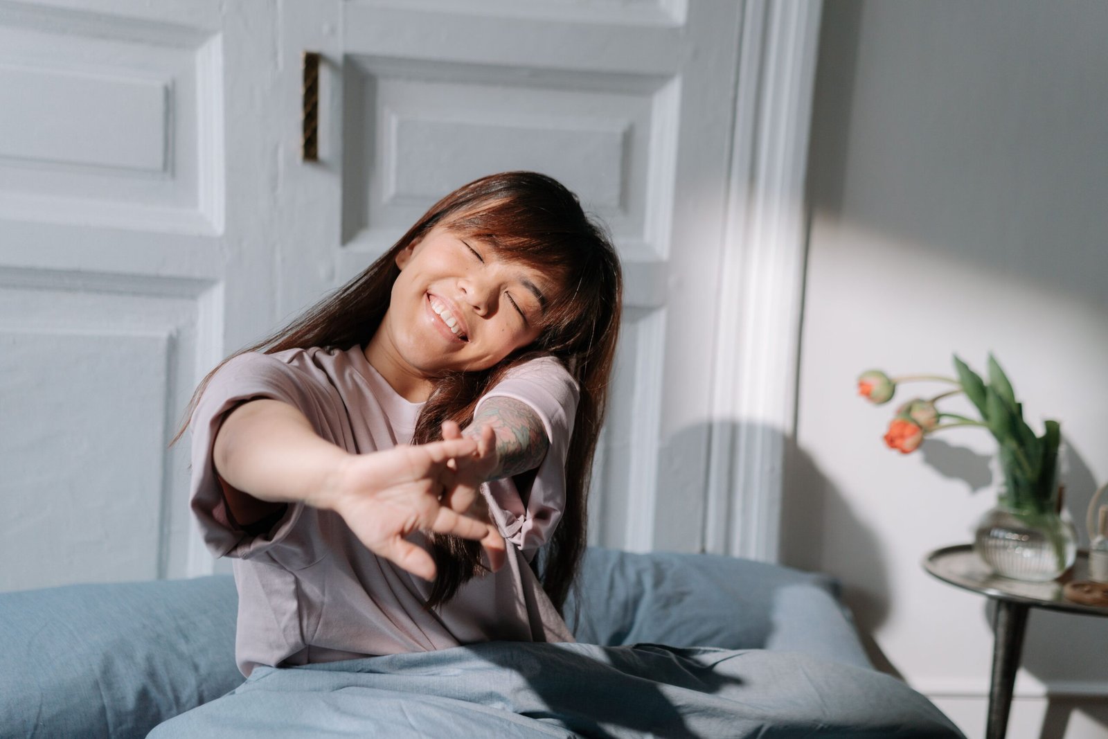 Woman stretching and smiling as she wakes up in a sunlit bedroom