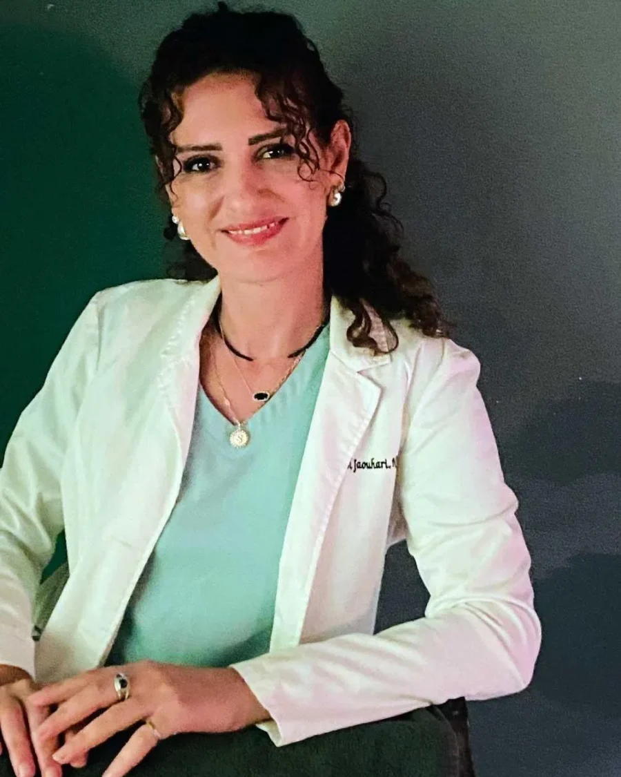Shahnaz El Jaouhari, NP, smiling in a white coat with a stethoscope embroidered name tag