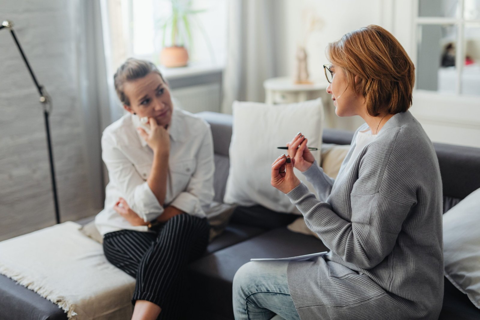 A provider in a grey cardigan takes notes and talks with a patient during a consultation in a bright, comfortable room