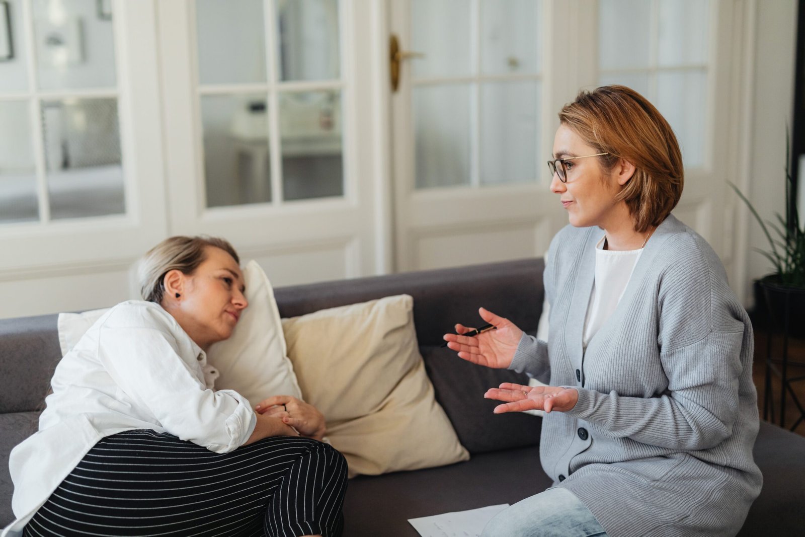 A provider gestures while explaining something to a patient listening thoughtfully on a couch